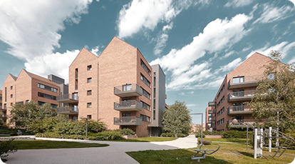 Red brick apartment buildings with balconies, greenery, and fitness equipment in landscaped area