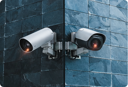 Two active security cameras mounted on a dark blue tiled corner wall