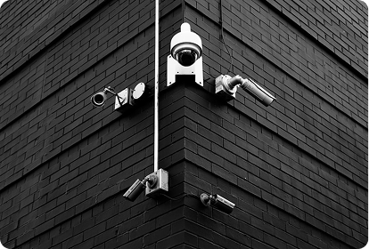 Corner of a brick building with six security cameras and a white conduit pipe
